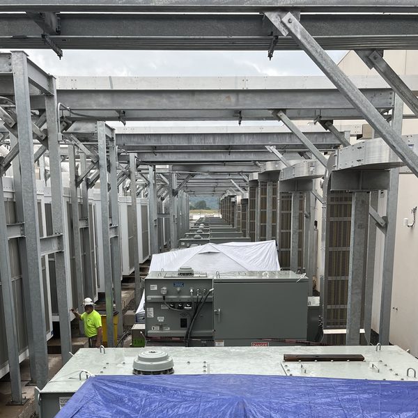 Rows of transformers under a steel canopy, with a worker in high-visibility clothing further down the line