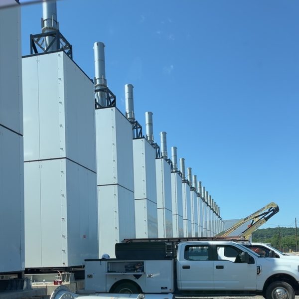 A line of tall outdoor equipment enclosures with exhaust stacks, and a service truck parked alongside