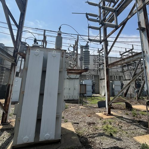 A transformer on its pad in a substation yard, with porcelain insulators and disconnect switches on the structures overhead