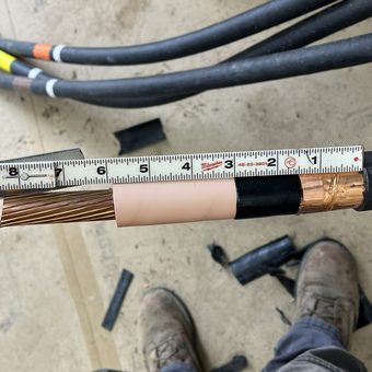 Medium voltage cable prep measured against a tape rule, showing the stranded conductor, stress-relief tubing and copper tape shield